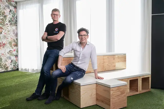 Zwei Gründer entspannt auf Holzmöbeln im kreativen Start-up-Büro mit Kunstrasen – modernes Imagefoto